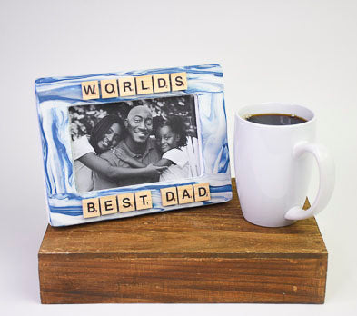 A blue and white marbled clay picture frame decorated with letter tiles spelling "WORLD'S BEST DAD