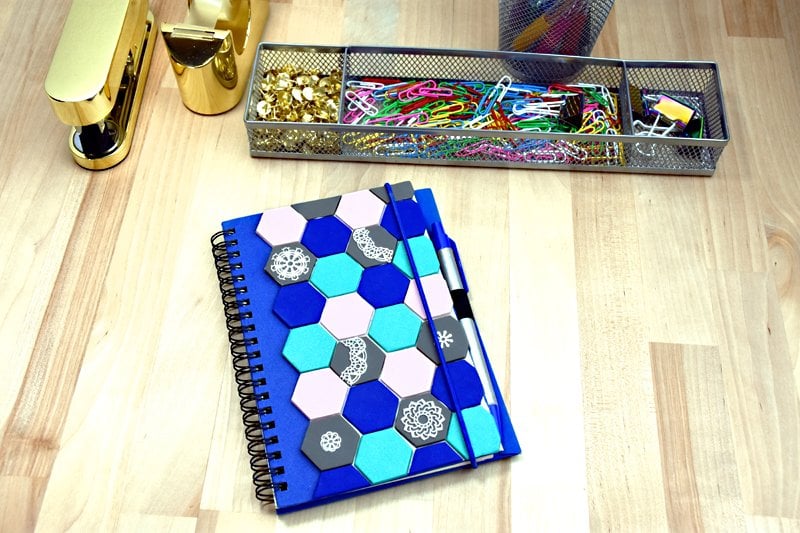 Spiral notebook with blue hexagon patterns next to gold stapler and tray of paper clips.