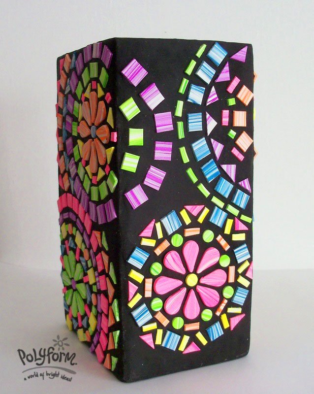A decorative handcrafted clay vase featuring a white base adorned with a variety of colorful three-dimensional geometric patterns.